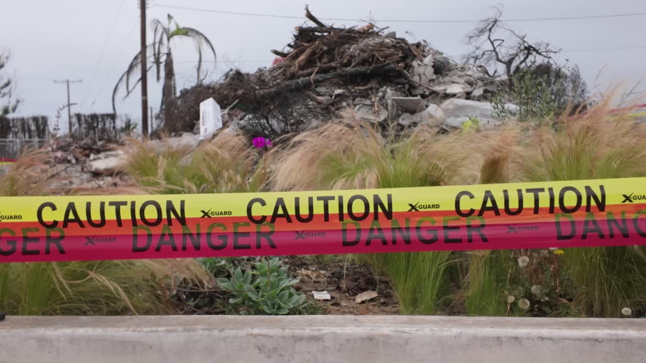 Gimbal close-up panning shot of caution tape surrounding fire debris after the Palisades Fire in Southern California. 4K