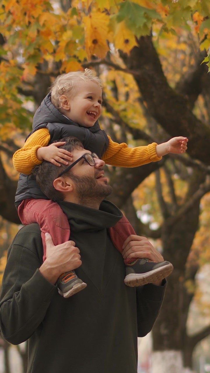 Padre che porta il figlio piccolo sulle spalle in un parco autunnale