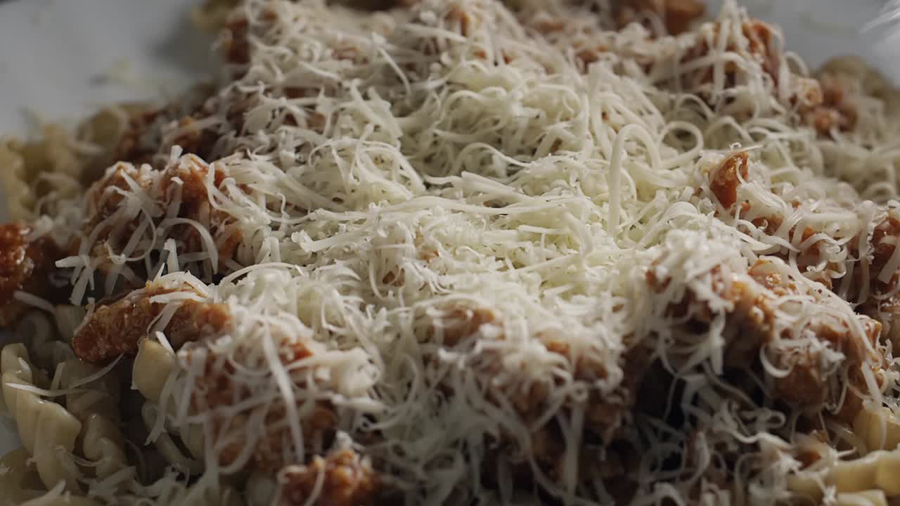 queso parmesano cayendo sobre pasta fusilli con salsa de carne, cámara lenta