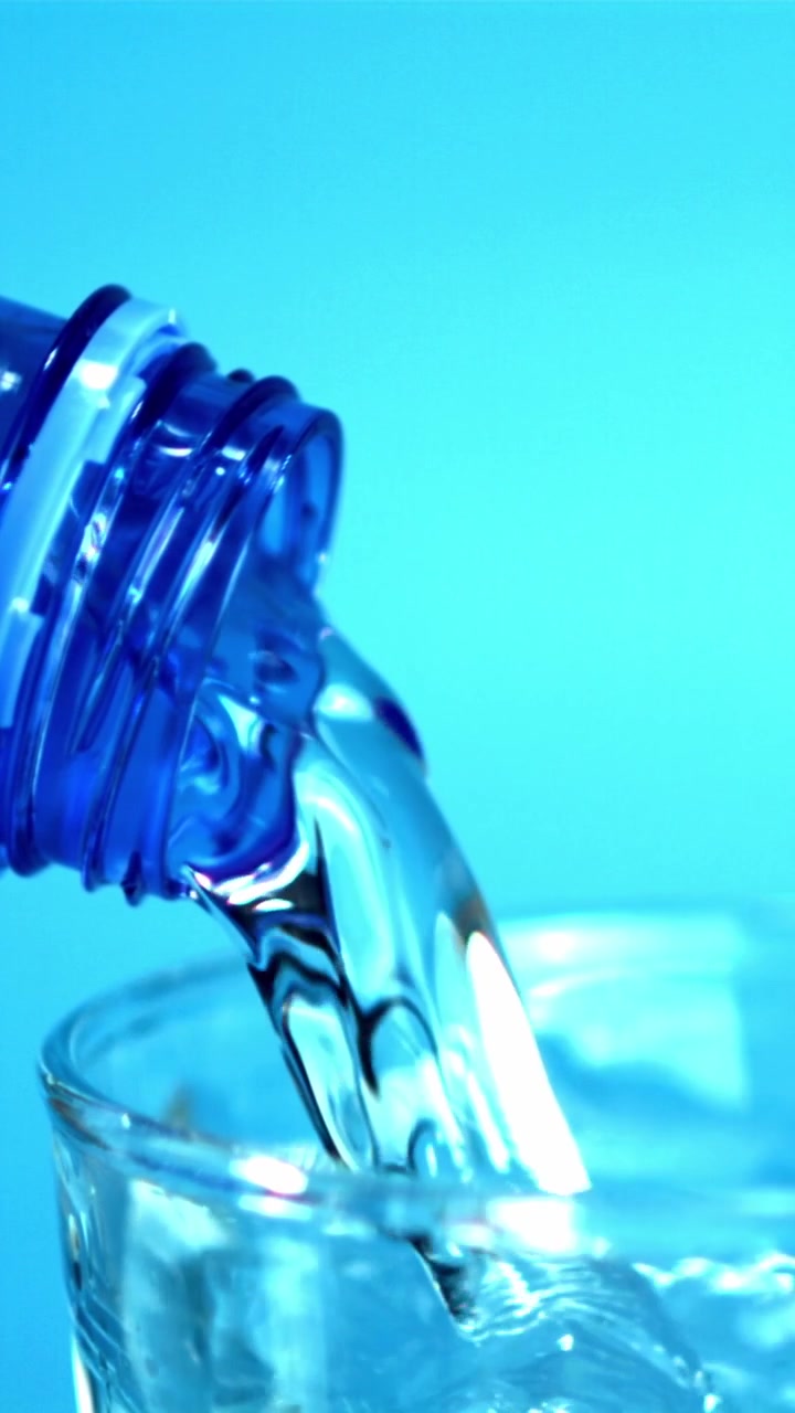 Klares Wasser fließt aus blauer Flasche in ein Glas