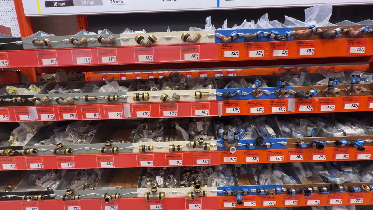 Panning shot across hardware store shelves displaying assorted plumbing fittings, including brass compression fittings, elbows, couplings, adapters, connectors and flexible hoses with retail price lab