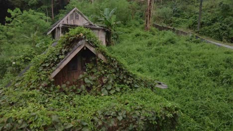 dolly tilt down shot drone view of old style wooden thai bungalow that is now taken over by jungle, derelict and unused due to the effects of the pandemic on travel and tourism in south east asia