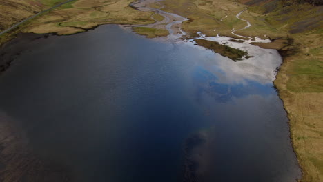 Fantástica-Toma-Aérea-Sobre-Un-Pequeño-Lago-Que-Revela-Las-Hermosas-Montañas-Ubicadas-En-El-Valle-De-Las-Tierras-Altas-De-Glencoe