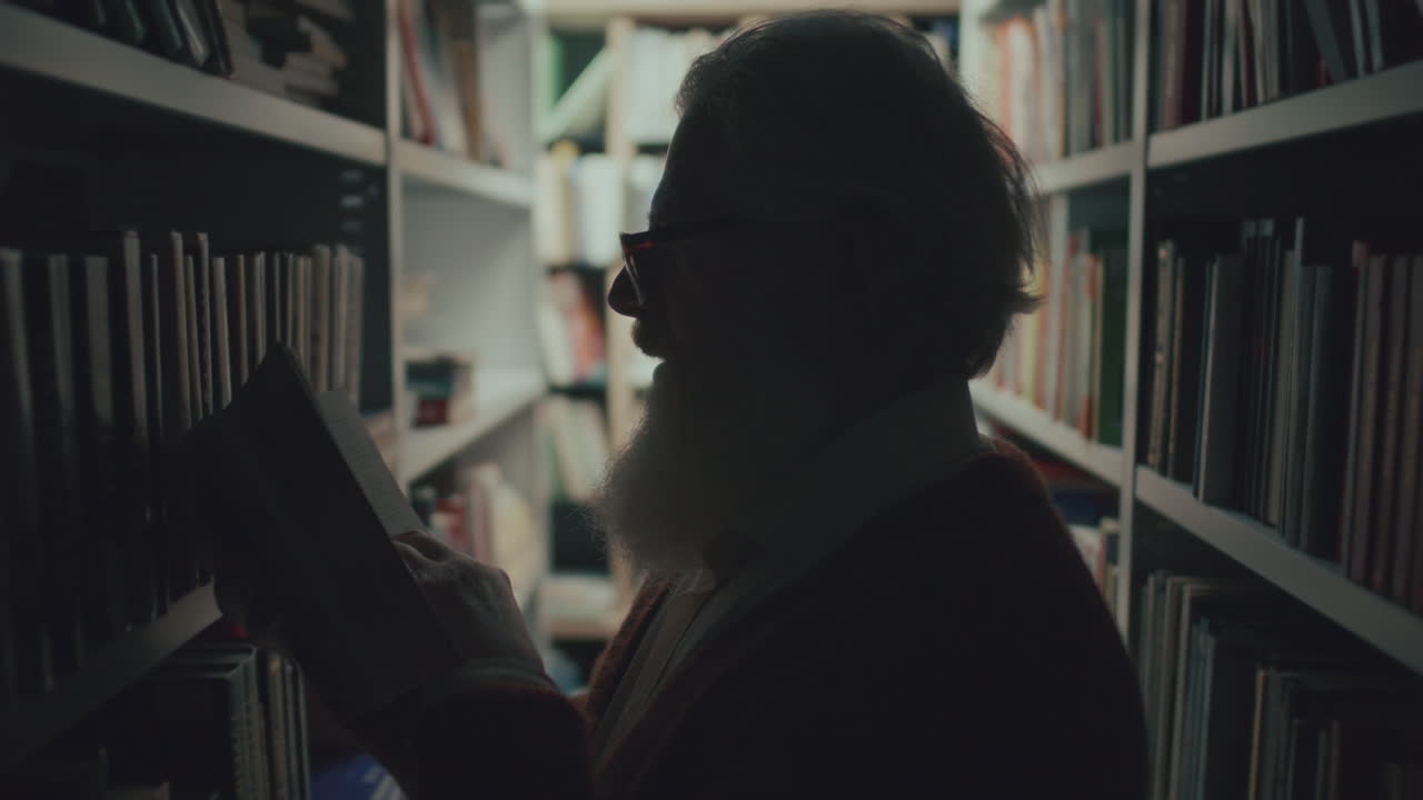 silueta de un hombre mayor leyendo un libro entre estantes en una biblioteca débilmente iluminada