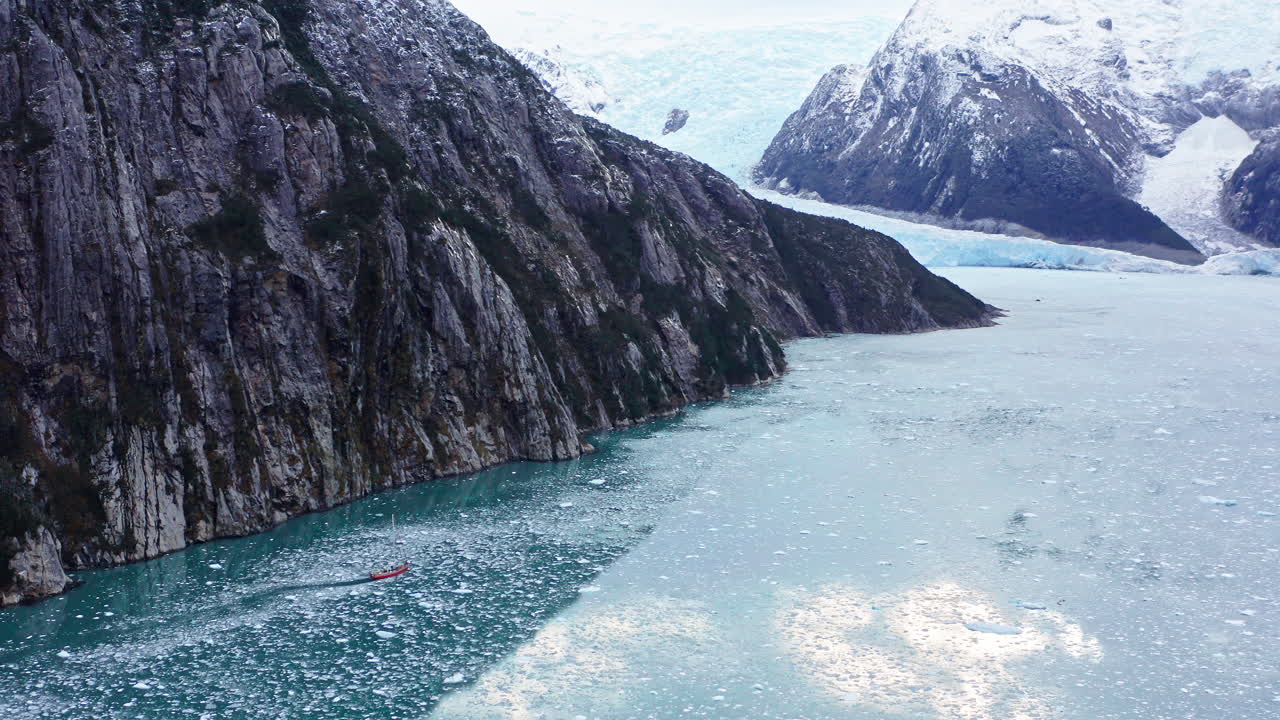 Boat Sailing Across The Glaciers Near Cape Horn On Hornos Island, Tierra del Fuego, South Chile. Aerial Drone Shot