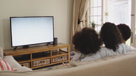 mixed race lesbian couple and daughter watching tv sitting on couch