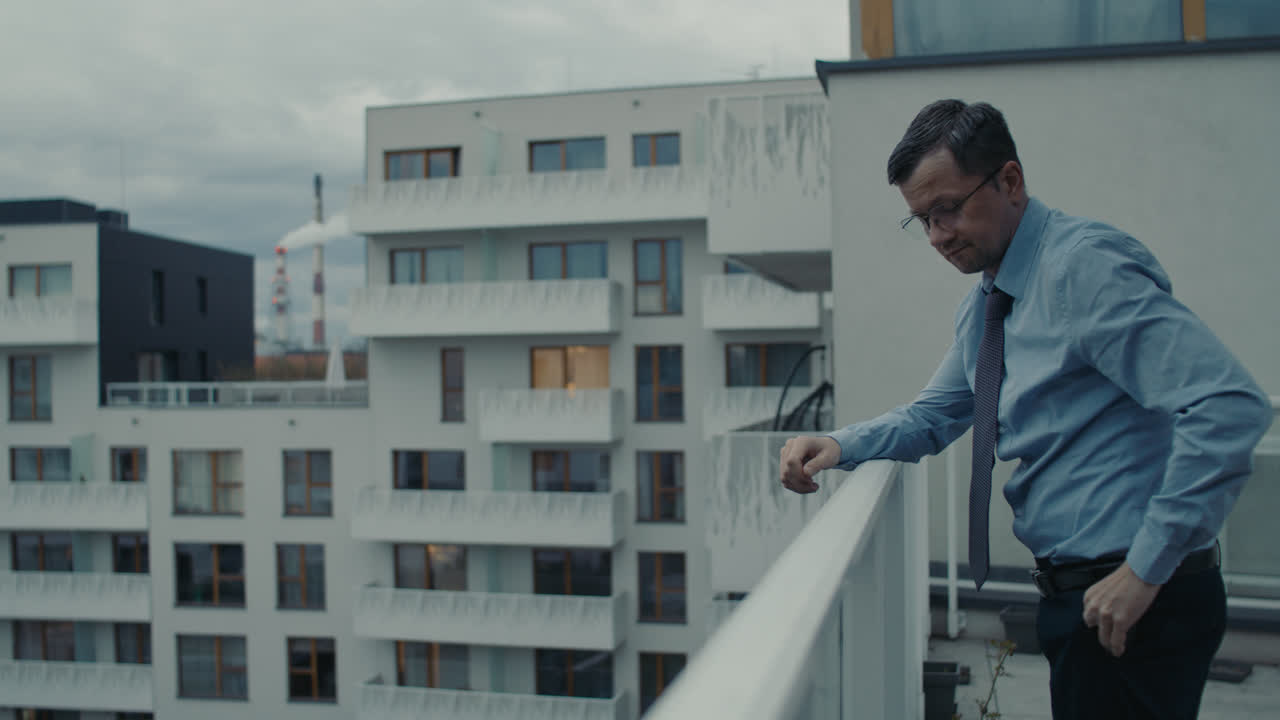 A sad man in a shirt smokes a cigarette on the balcony