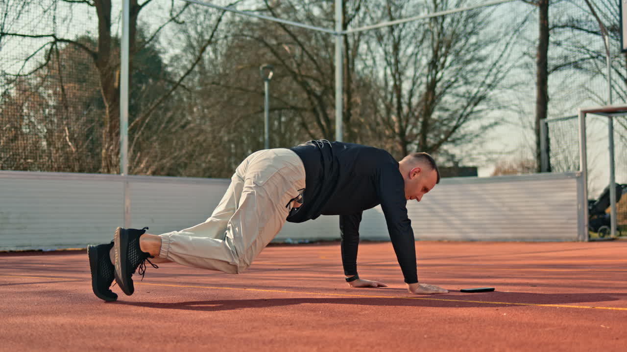 Un uomo sta facendo sport su un campo sportivo all'aperto. In estate, si dedica al proprio corpo svolgendo esercizi per la tonificazione e il miglioramento della forma fisica.