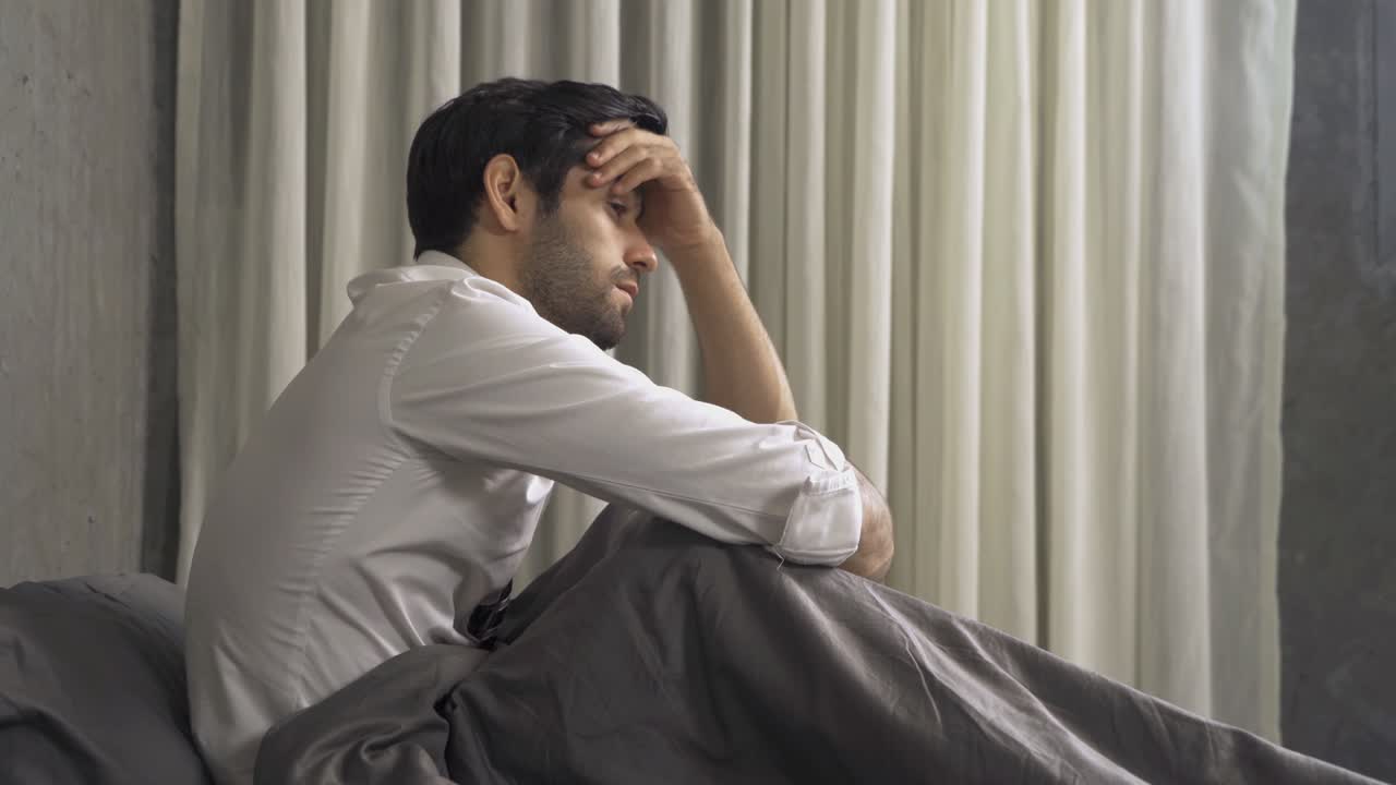 우울한 외로운 비즈니스 중동 남자는 직장에서 해고됩니다. 아침 일찍 집에서 침실에서 창문이있는 침대에 앉아 있습니다. 격리 생활 방식. 불행한 삶.