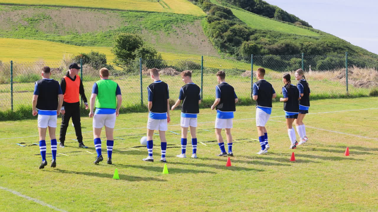 Male and female soccer players warming up and practicing bouncing with head with coach on pitch