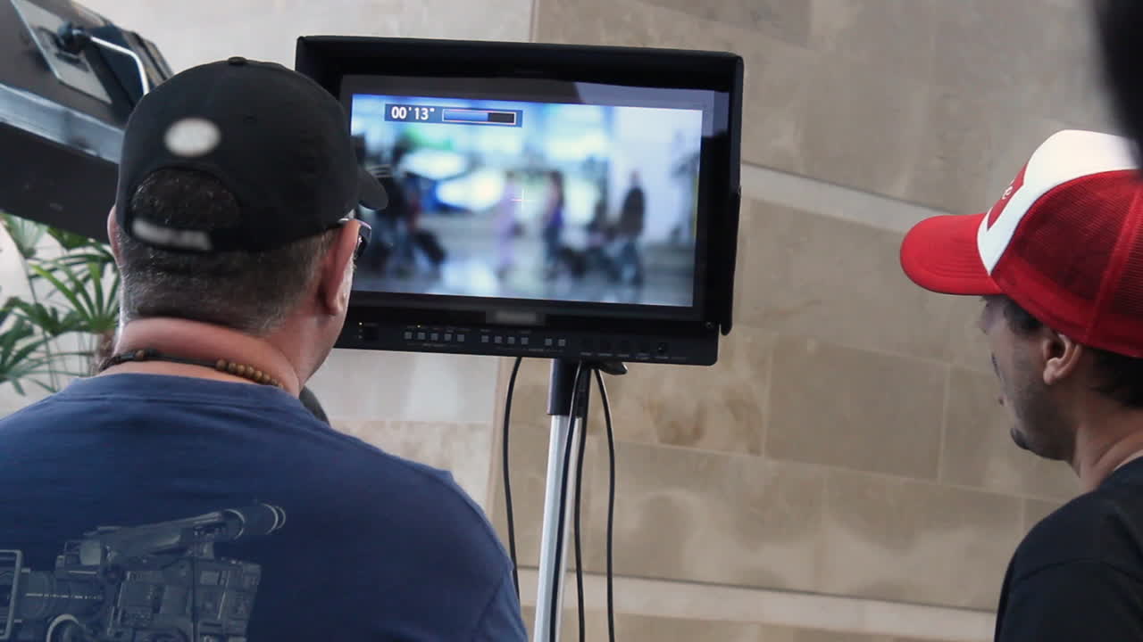Director and assistant review the recorded material of people walking on a monitor while on shooting set