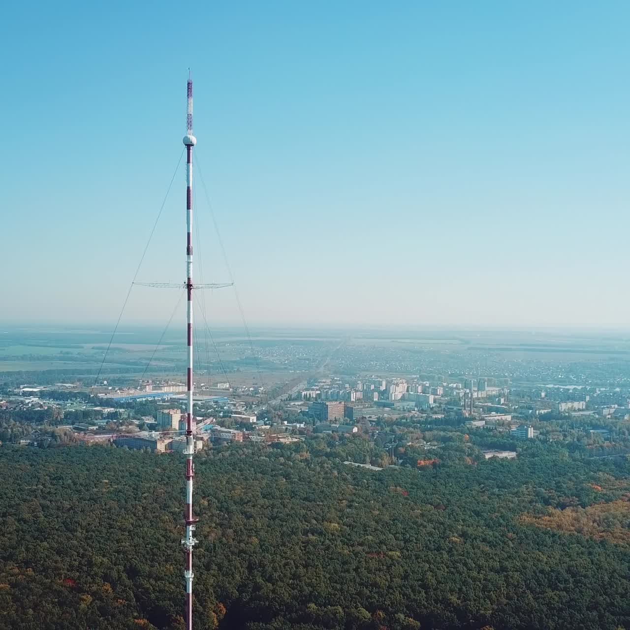 one telecommunication tower is located near the city in the background of the forest. Camera motion back