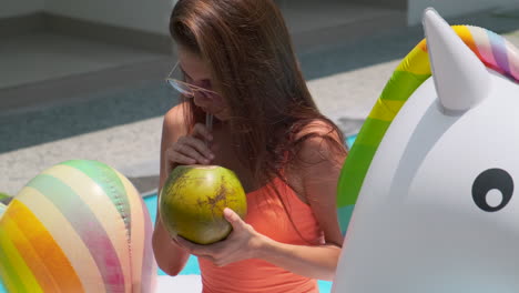 mujer bebiendo agua de coco en un flotador de piscina unicornio
