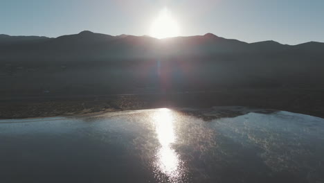 Luftaufnahme-über-Wasser-In-Richtung-Wüstenberglandschaft-Und-Sonnenuntergang-In-Der-Ferne