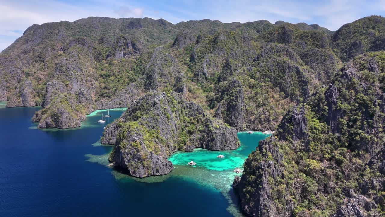 Aerial view of Twin Lagoon in Coron, Philippines, highlighting jagged limestone cliffs, lush greenery, turquoise waters, and moored boats in a secluded tropical paradise surrounded by deep blue sea