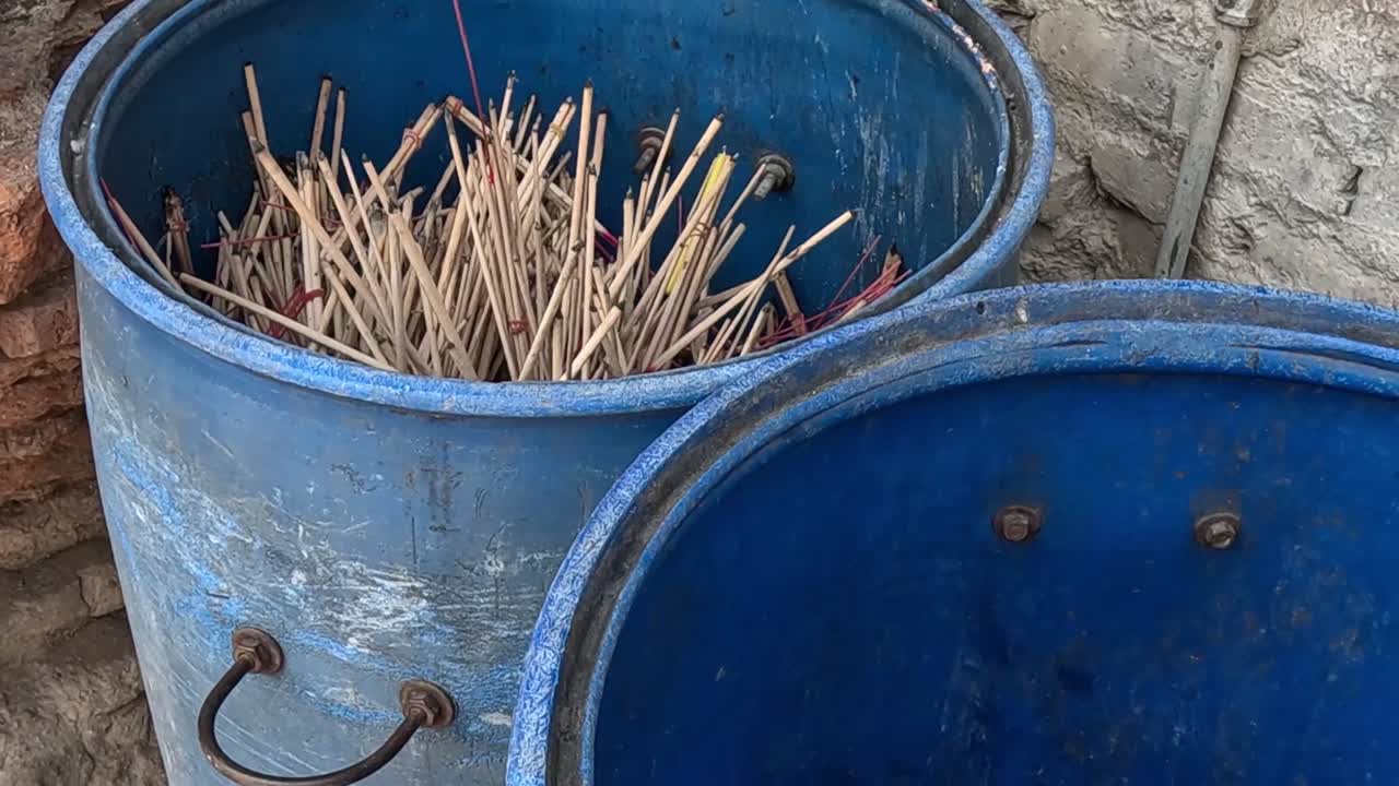 Two blue buckets filled with wooden sticks against a brick wall backdrop.