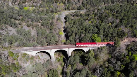 antena: viejo tren rojo y blanco en un bosque cruzando un antiguo viaducto en el sur de francia