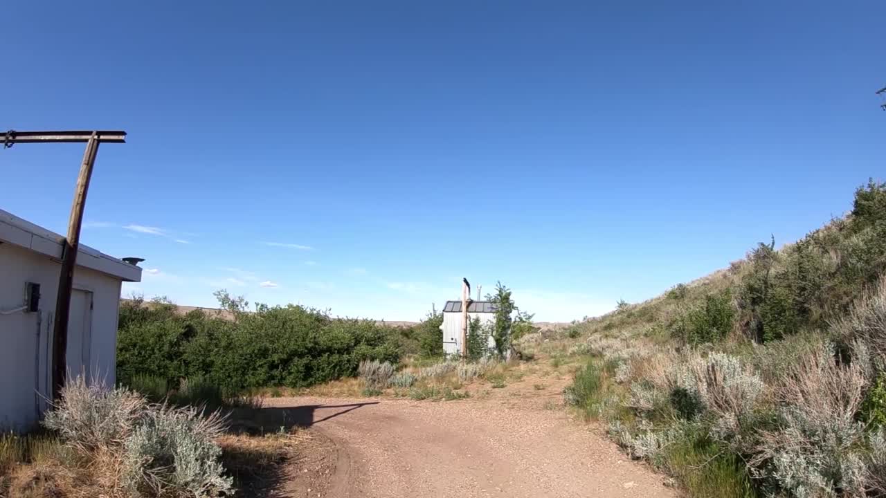 Two old small building next to a lake down a long gravel road in the country on a sunny day.