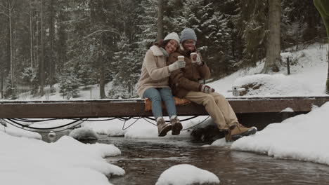 una pareja disfrutando de café en un puente de madera nevado