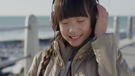 Close-Up-Retrato-Linda-Niña-Asiática-Con-Auriculares-Sonriendo-Bailando-Disfrutando-Escuchando-Música-En-La-Playa-Junto-Al-Mar