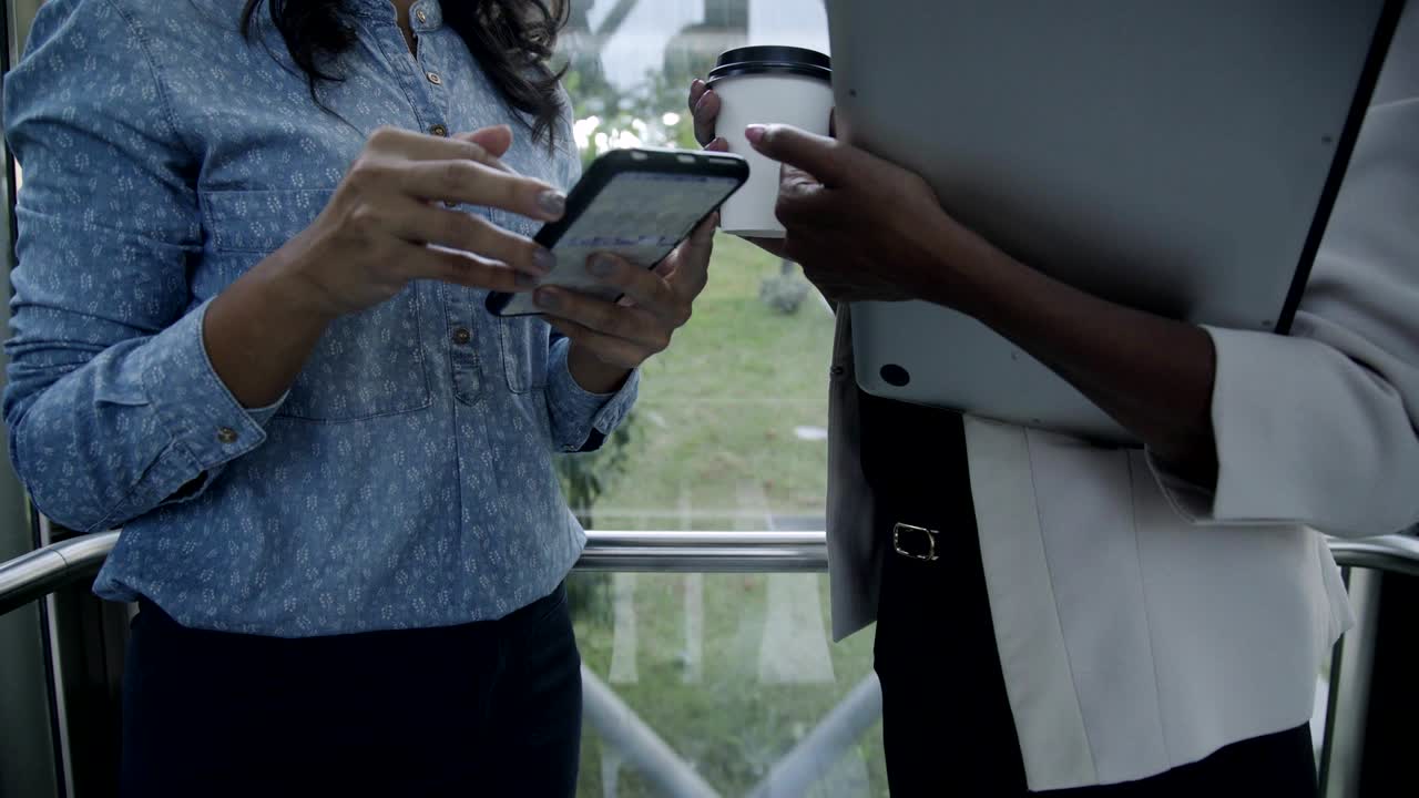 Female business agents with gadgets and coffee to go in elevator