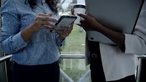 female business agents with gadgets and coffee to go in elevator