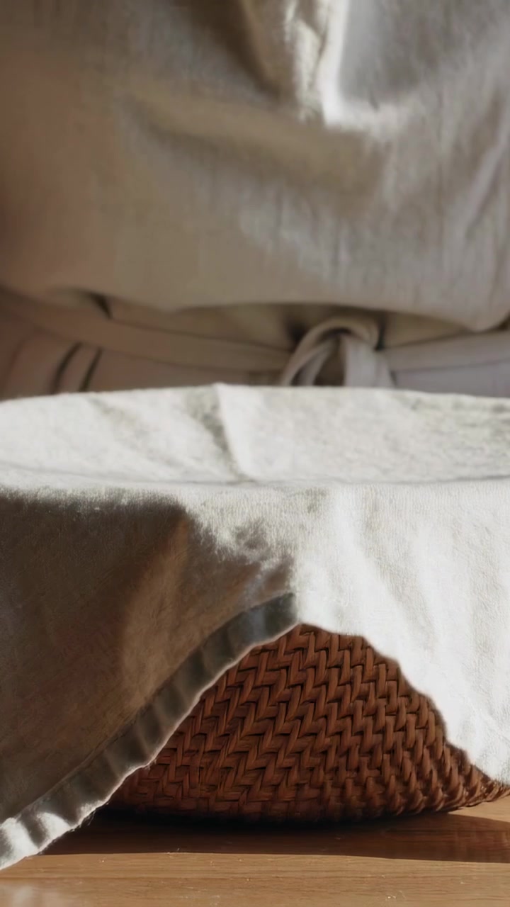 Vertical video: Revealing pale linen shifting over woven basket on wood floor, exposing tied cord