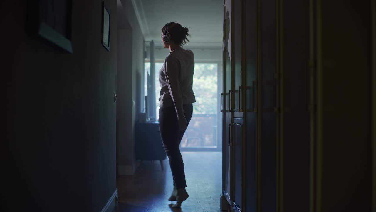 feliz mujer hermosa con auriculares baila a través de su pasillo de apartamento. alegre chica auténtica escuchando música en casa bailando de buen humor. toma completa