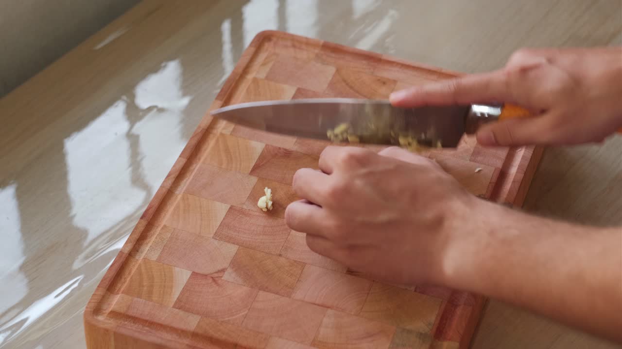 Finely Cutting Garlic on Wooden Chopping Board in Well-Lit Room – Static Shot