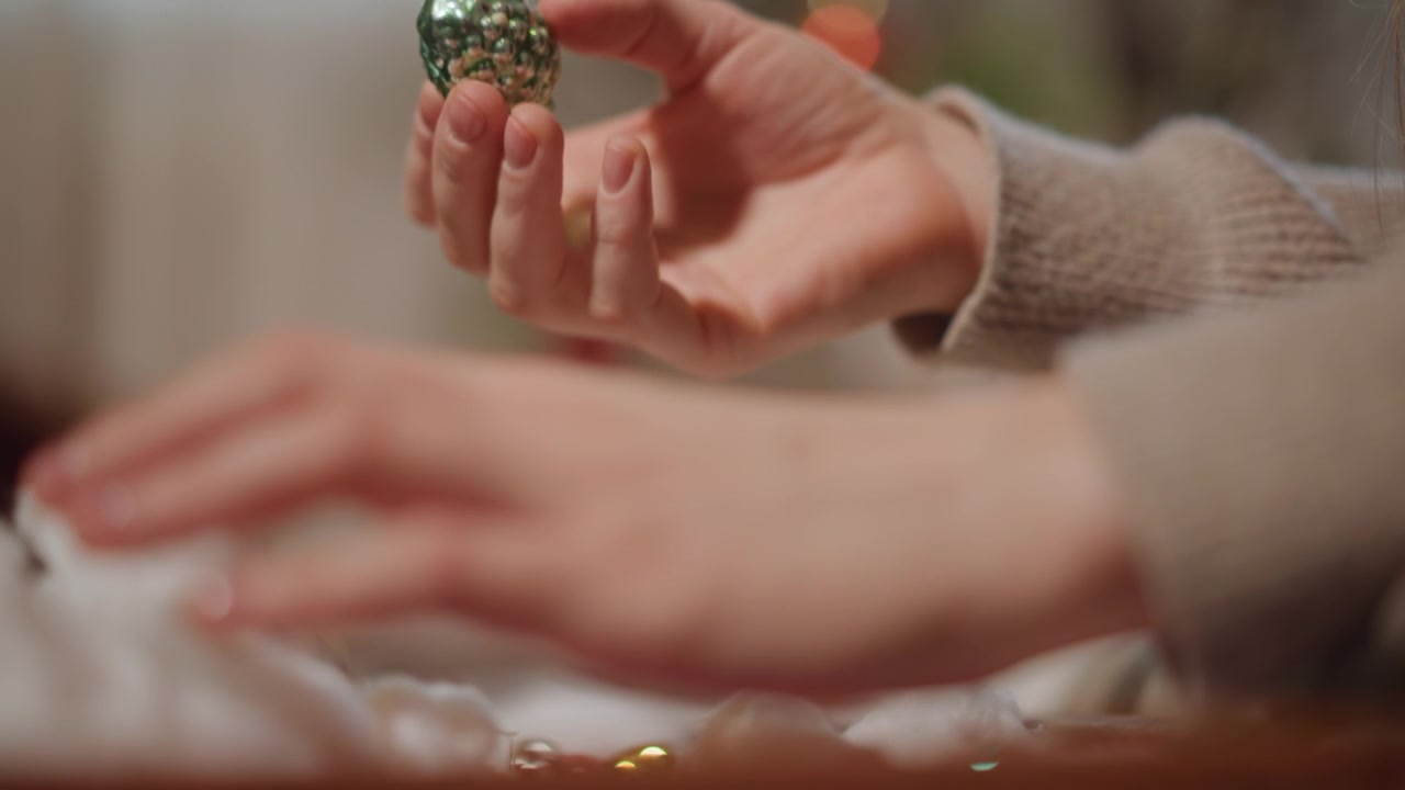 Scena festiva dettagliata. Focus sulle mani che sistemano decorazioni natalizie con una calda atmosfera di festa. Scatto intimo che cattura le mani che posizionano delicatamente gli ornamenti in una scatola di legno tra le luci natalizie.