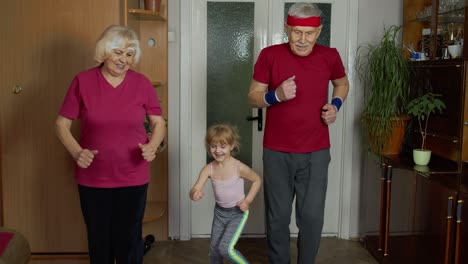 Granddaughter-and-mature-grandparents-in-sportswear-making-sports-jogging-workout-exercises-at-home