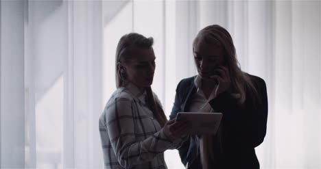 Female-Colleagues-Discussing-Over-Digital-Tablet-In-Office