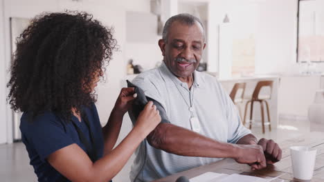 female healthcare worker checking the blood pressure of a senior man during a home visit, close up