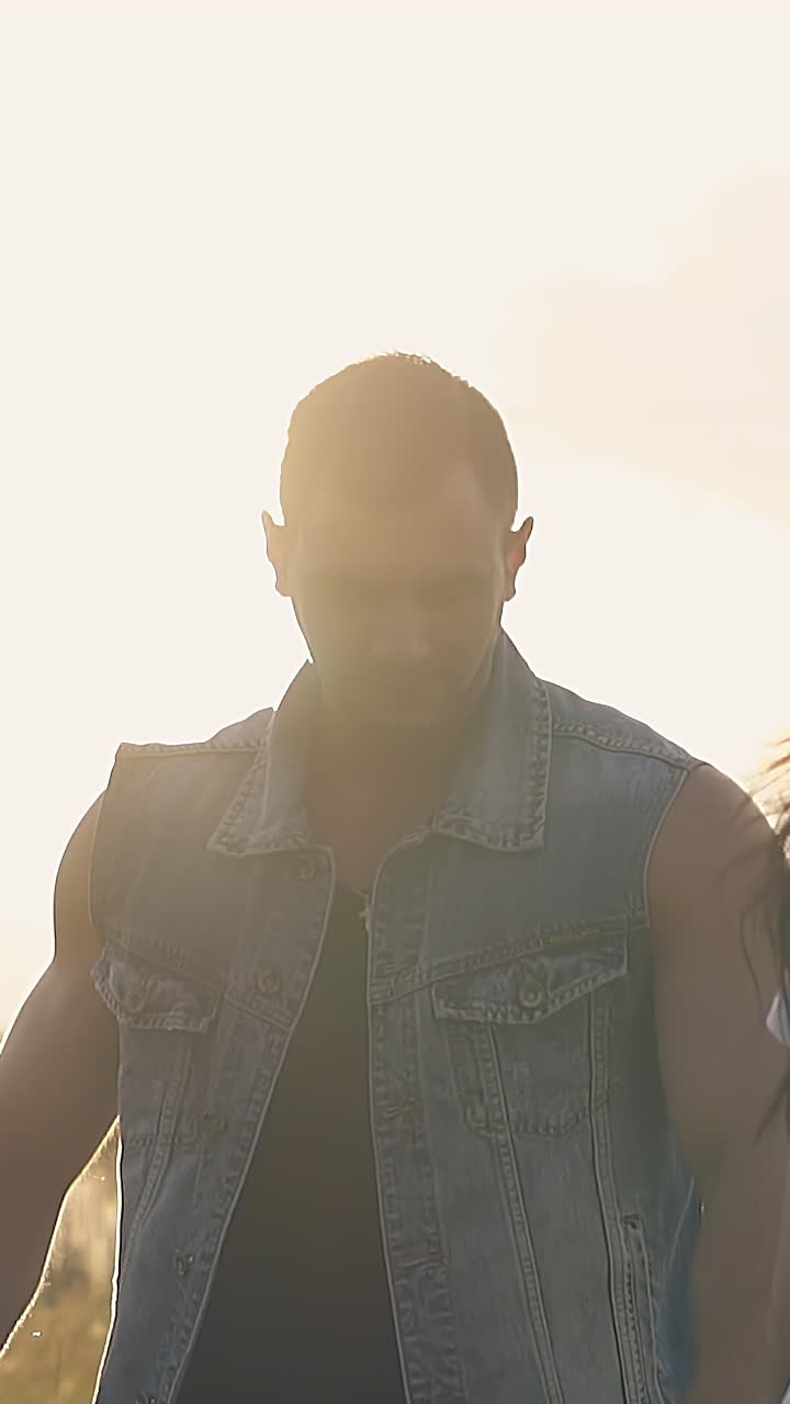 close view young couple silhouette lit by summer evening sun walks on field with joining hands slow motion
