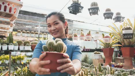 portrait of beautiful young asian girl showing indoor cactus plant in flowerpot