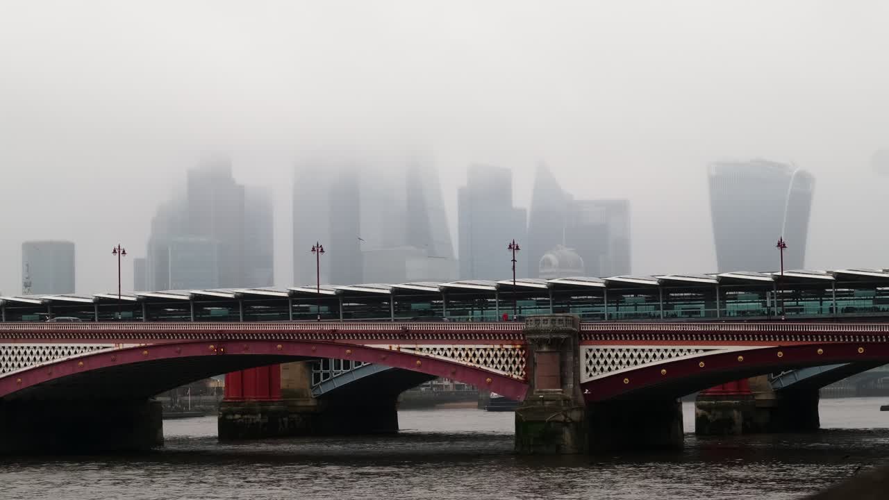 View of the Blackfriars Bridge on the river thames with iconic London financial district skyscrapers in the background during a rainy misty day.