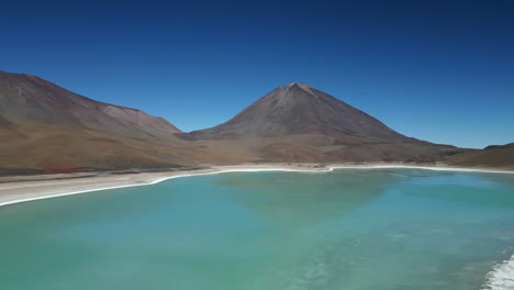 Aerial-drone-panning-shot-over-a-large-frozen-lake-surrounded-by-mountain-range-in-Bolivia-on-a-sunny-day