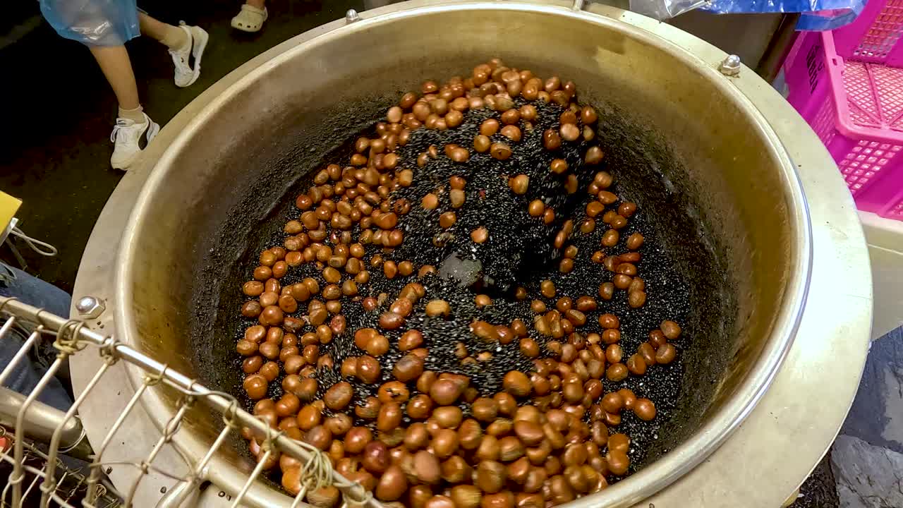 Chestnuts stir-roasted with black gravel in a metal pan, vibrant street market, overhead view