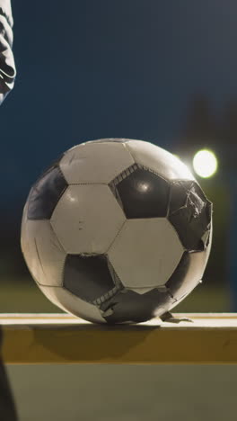 cerca de alguien sentado en un banco con una pelota de fútbol gastada a su lado, el viento mueve la pelota ligeramente, y la persona la estabiliza para evitar que caiga