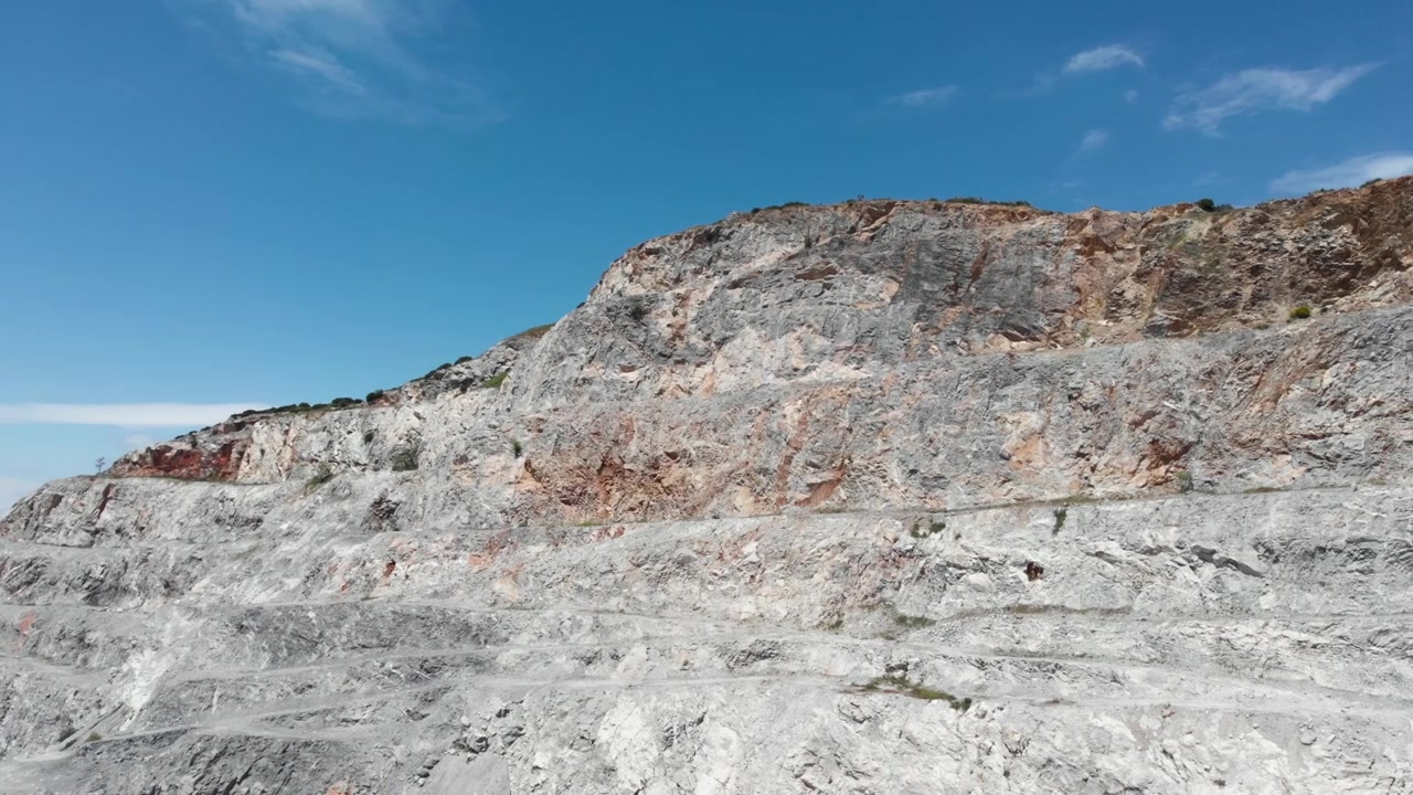 Laaja ilmakuva suuresta louhoksesta, joka vangitsee sen karut, kerrokselliset kalliomuodostelmat kirkkaan sinisen taivaan alla. Hyödyllinen geologisiin tutkimuksiin tai teollisuusprojekteihin.