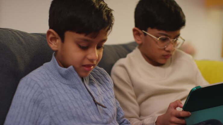 Due ragazzi seduti sul divano di casa che giocano o guardano contenuti in streaming su tablet digitali 17