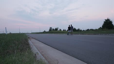 wide static shot of male skateboarder and friend checking phone footage at empty road in usa