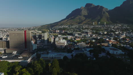 Aerial-footage-of-buildings-in-town.-Rocky-peaks-of-mountain-massive-in-background.-Clear-sky-on-sunny-day.-Cape-Town,-South-Africa