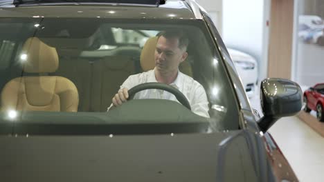 Client-in-white-shirt-sit-in-car-salon,-want-buy-new-automobile-in-showroom