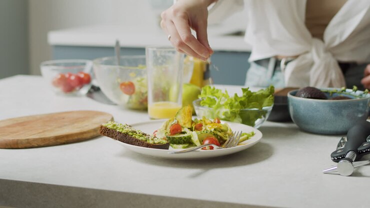 Close Up Of Woman Hand Adding Various Seeds Into Plate With Fresh Salad And Avocado Toast