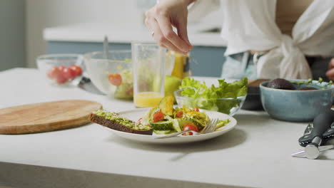 primer plano de la mano de la mujer agregando varias semillas en el plato con ensalada fresca y tostadas de aguacate