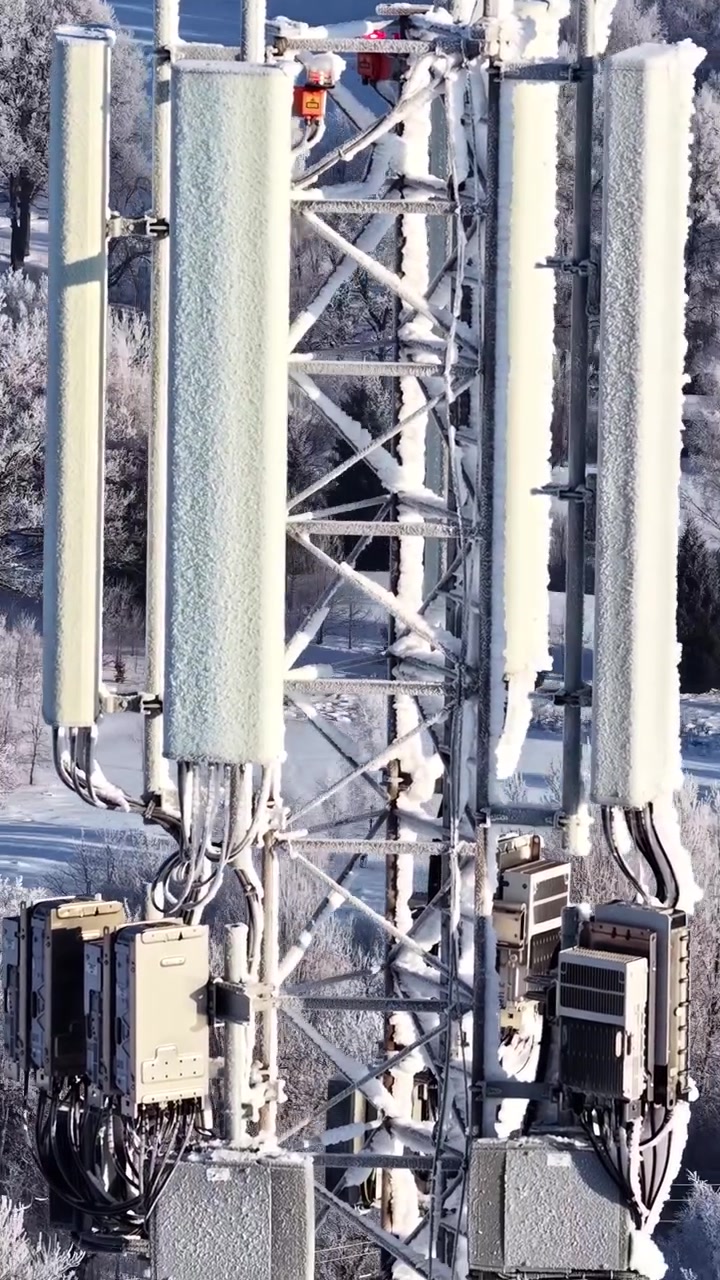 Antenne di una torre di telecomunicazioni coperte di brina sopra una foresta innevata, orbita verticale del drone.