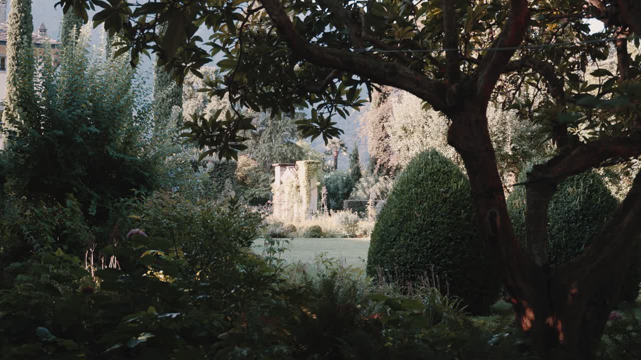 Guarda attraverso il giardino verdeggiante della famosa location per matrimoni Villa Balbiano, verso un particolare di un antico cancello storico in pietra
