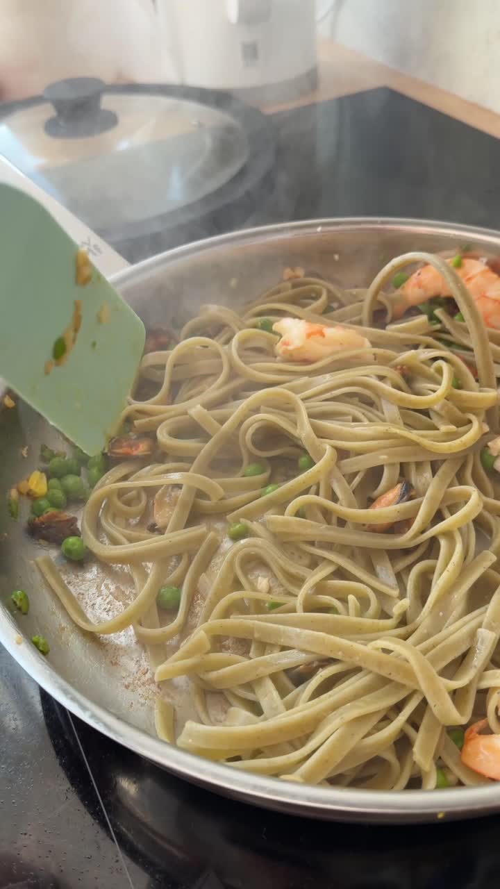 フライパンでエビ、ムール貝、エンドウ豆が入った生パスタをかき混ぜる様子。