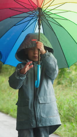 kid playfully spins multicolored parasol. boy spends time in fresh air in park despite cold rainy weather. childish playful mood in damp weather